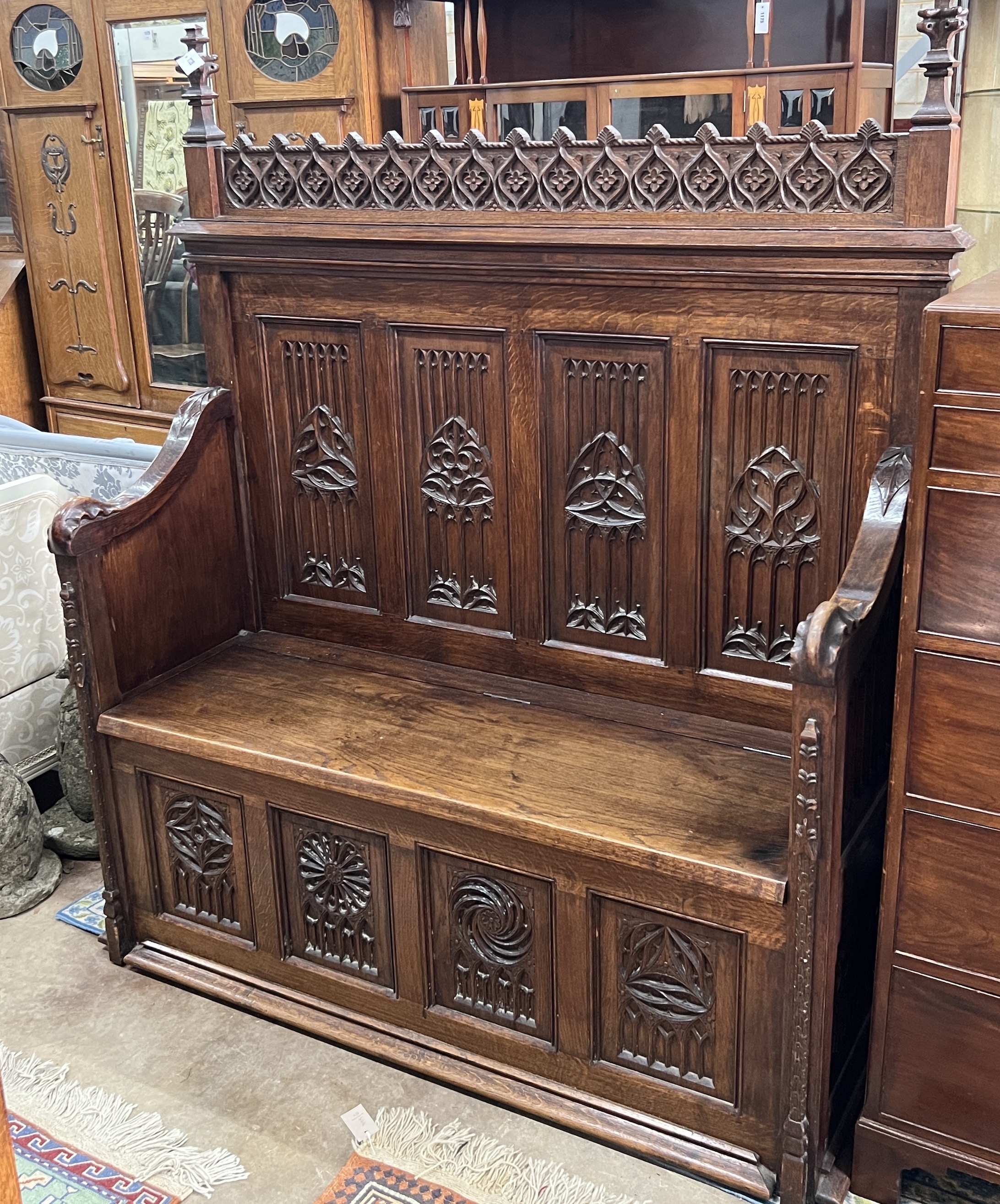 An early 20th century carved oak Gothic Revival settle with hinged box seat, width 137cm, depth 49cm, height 160cm